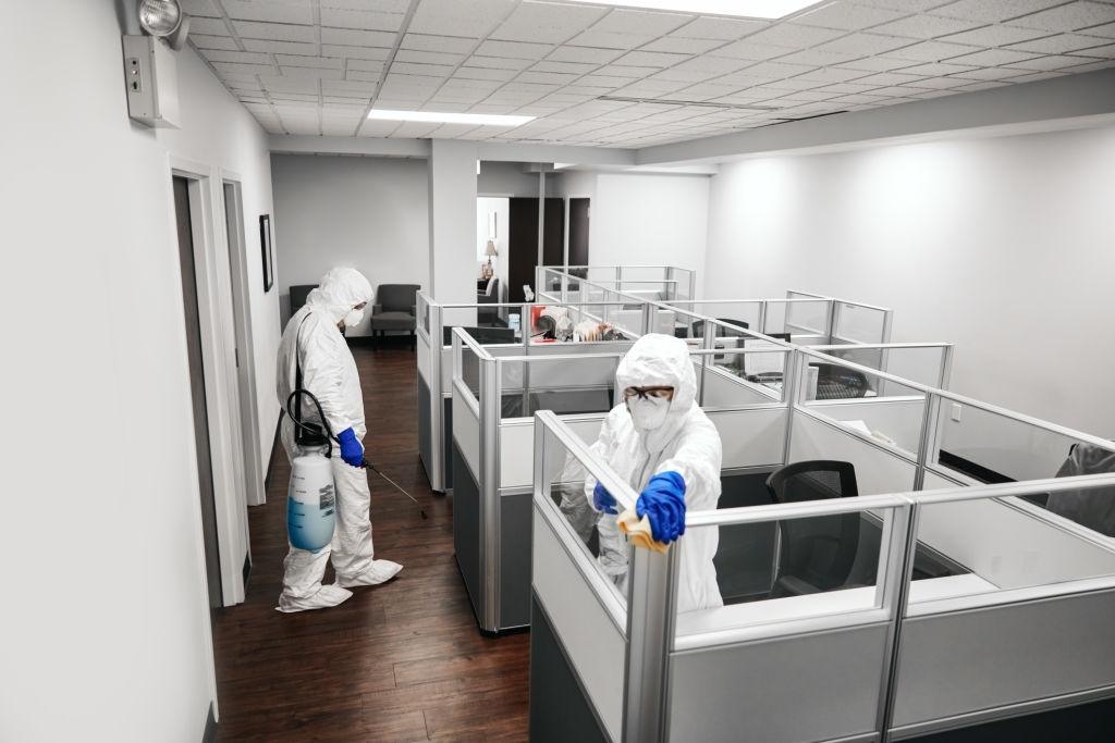 Two people in protective workwear cleaning and disinfecting offices.